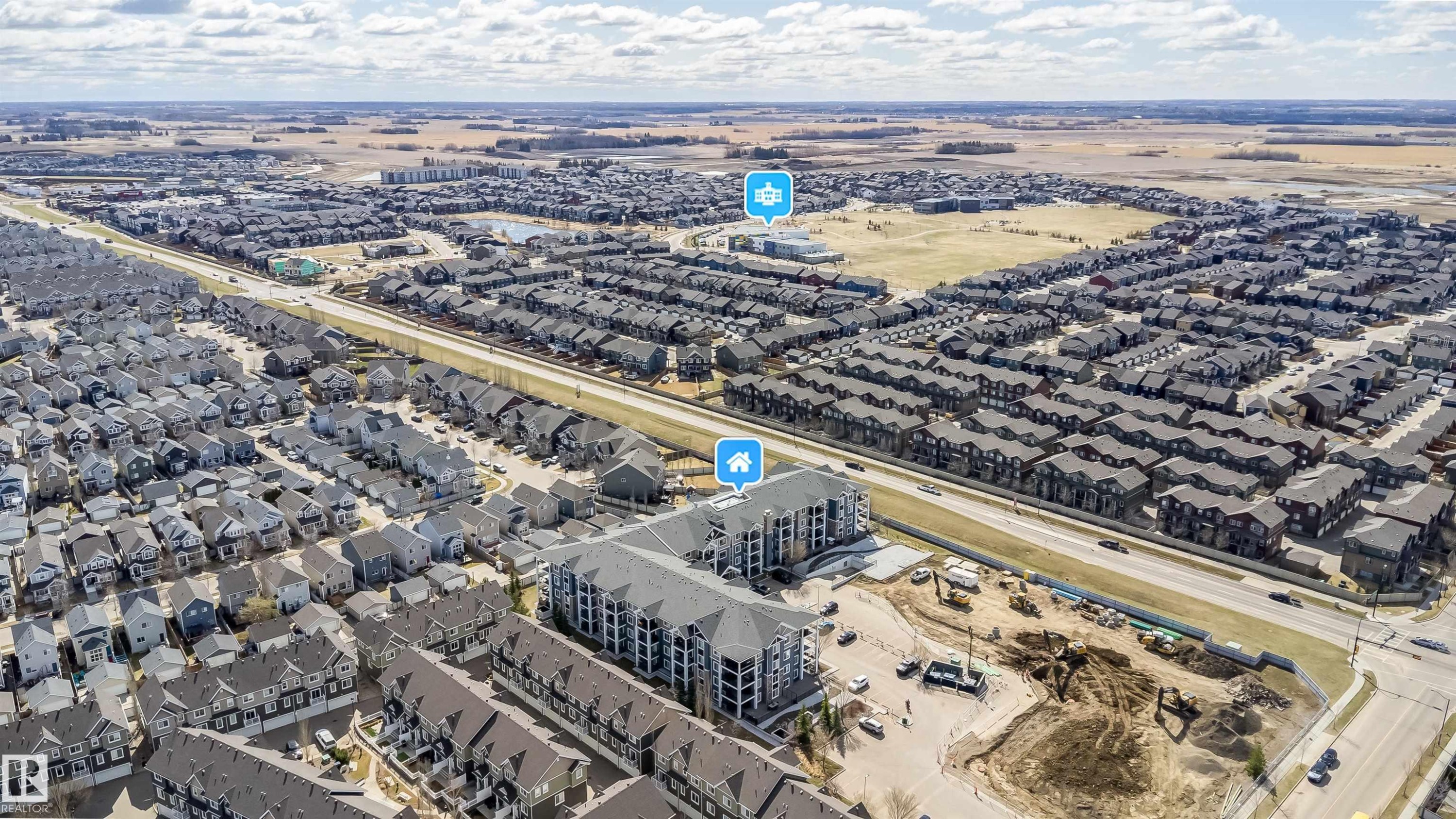 Expansive aerial perspective showcasing a developed residential neighborhood with a multi-story apartment building, single-family homes, and a commercial road - 421 4008 Savaryn Drive, Edmonton, AB - Outdoor With View