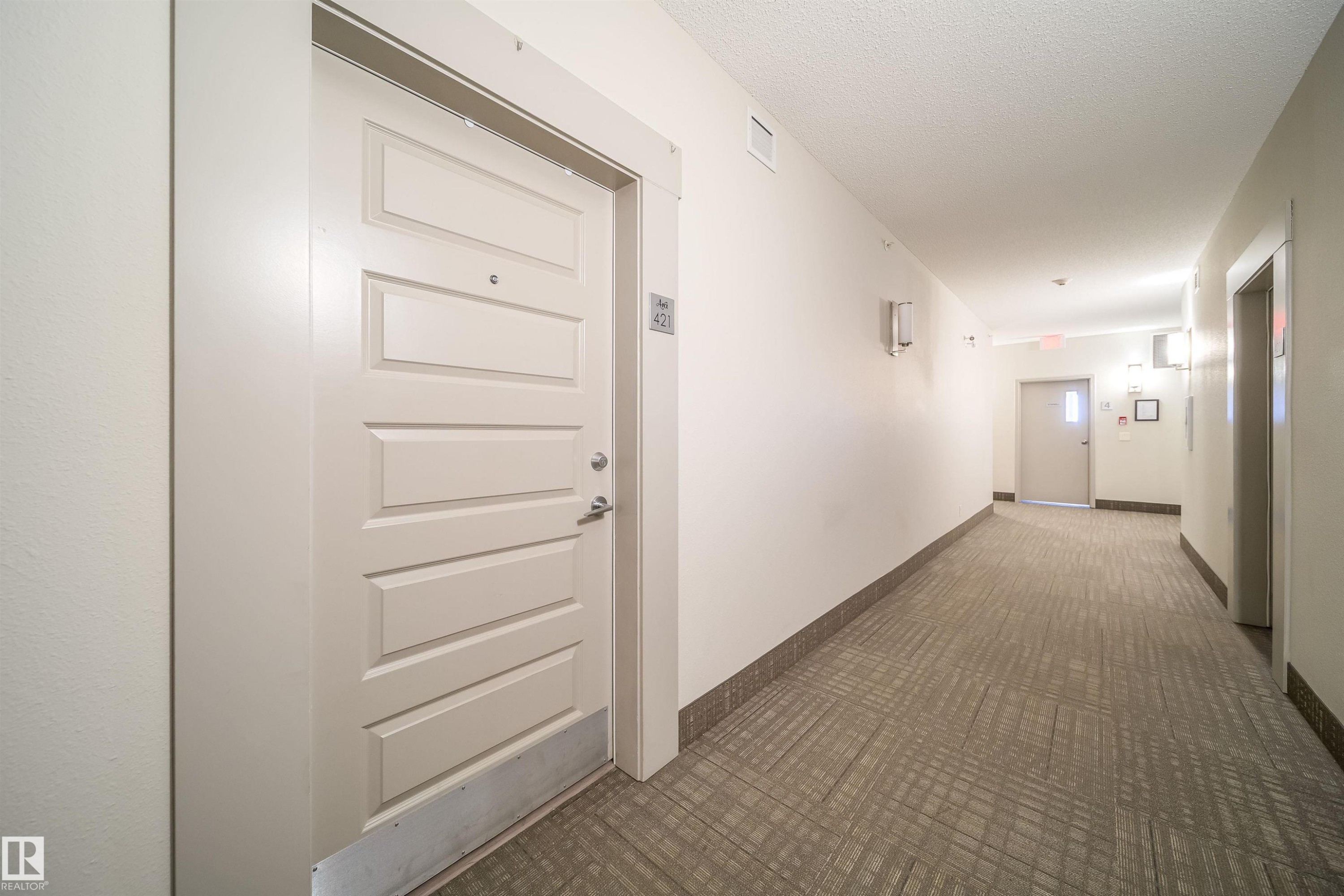 Corridor featuring a textured carpet runner, white paneled doors, and wall-mounted light fixtures - 421 4008 Savaryn Drive, Edmonton, AB - Indoor Photo Showing Other Room