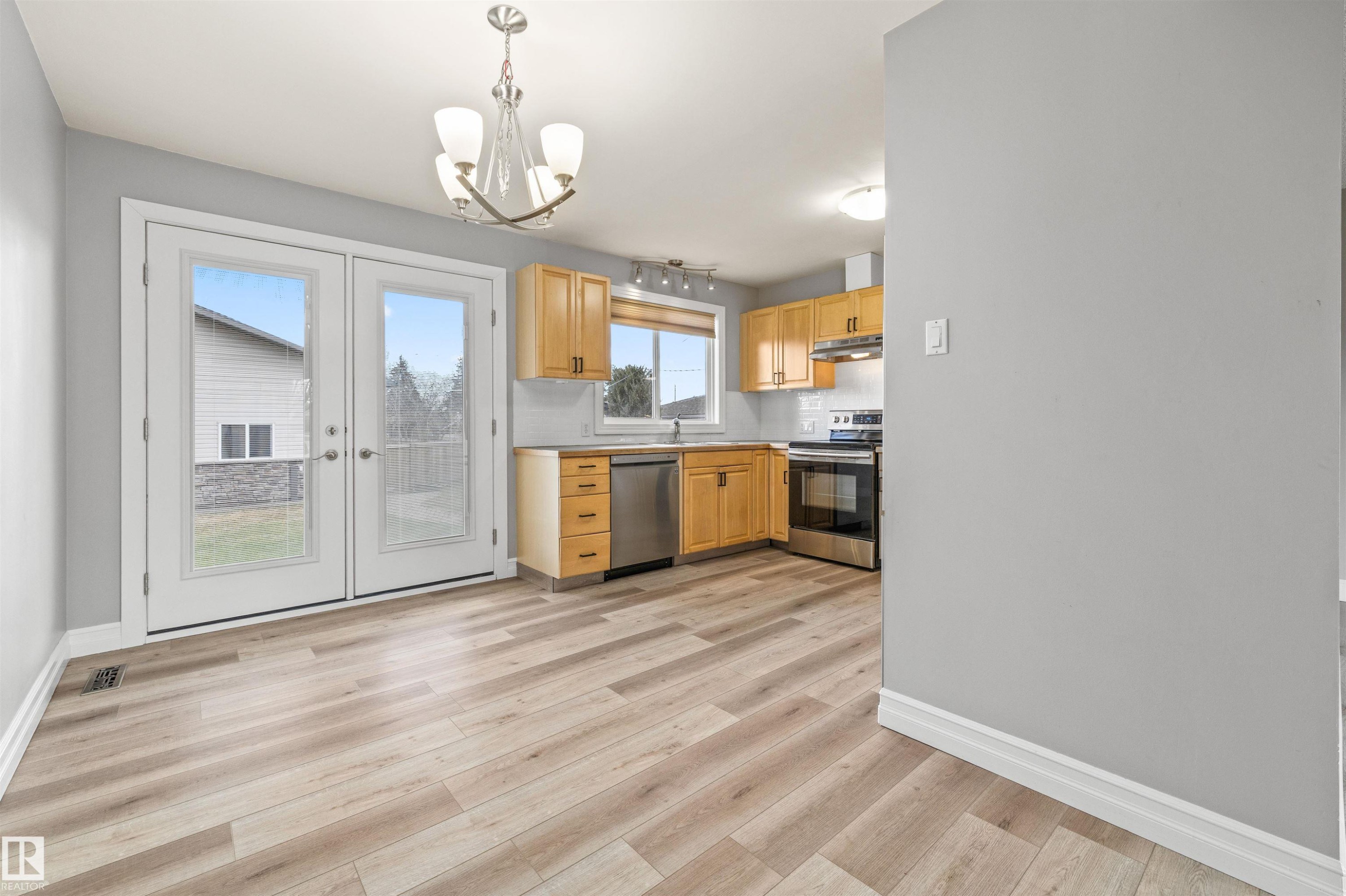 Open-concept space featuring light wood-finish flooring, a contemporary chandelier, and French doors - 7927 71 Avenue, Edmonton, AB - Indoor Photo Showing Kitchen