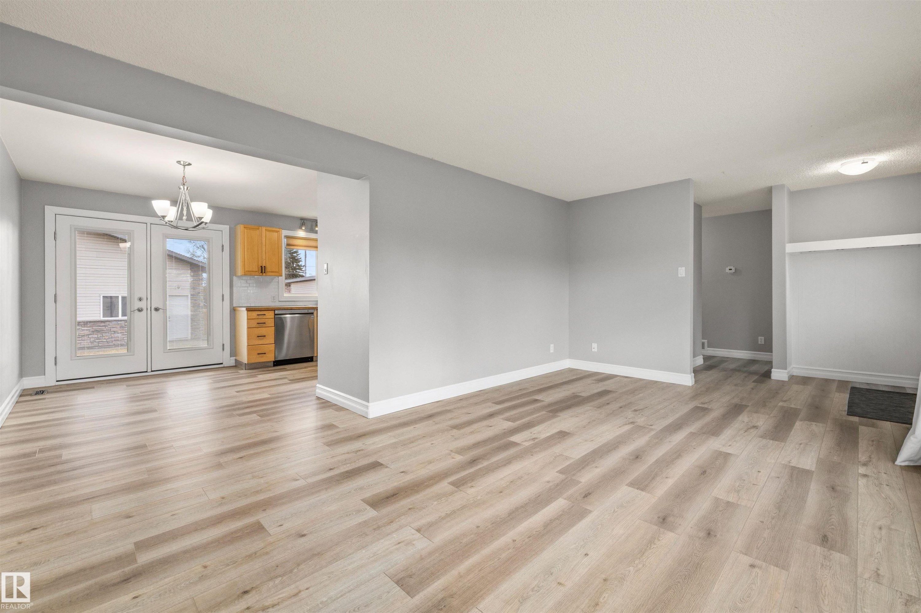 Spacious open-concept living area featuring light wood-finish flooring and neutral gray walls - 7927 71 Avenue, Edmonton, AB - Indoor