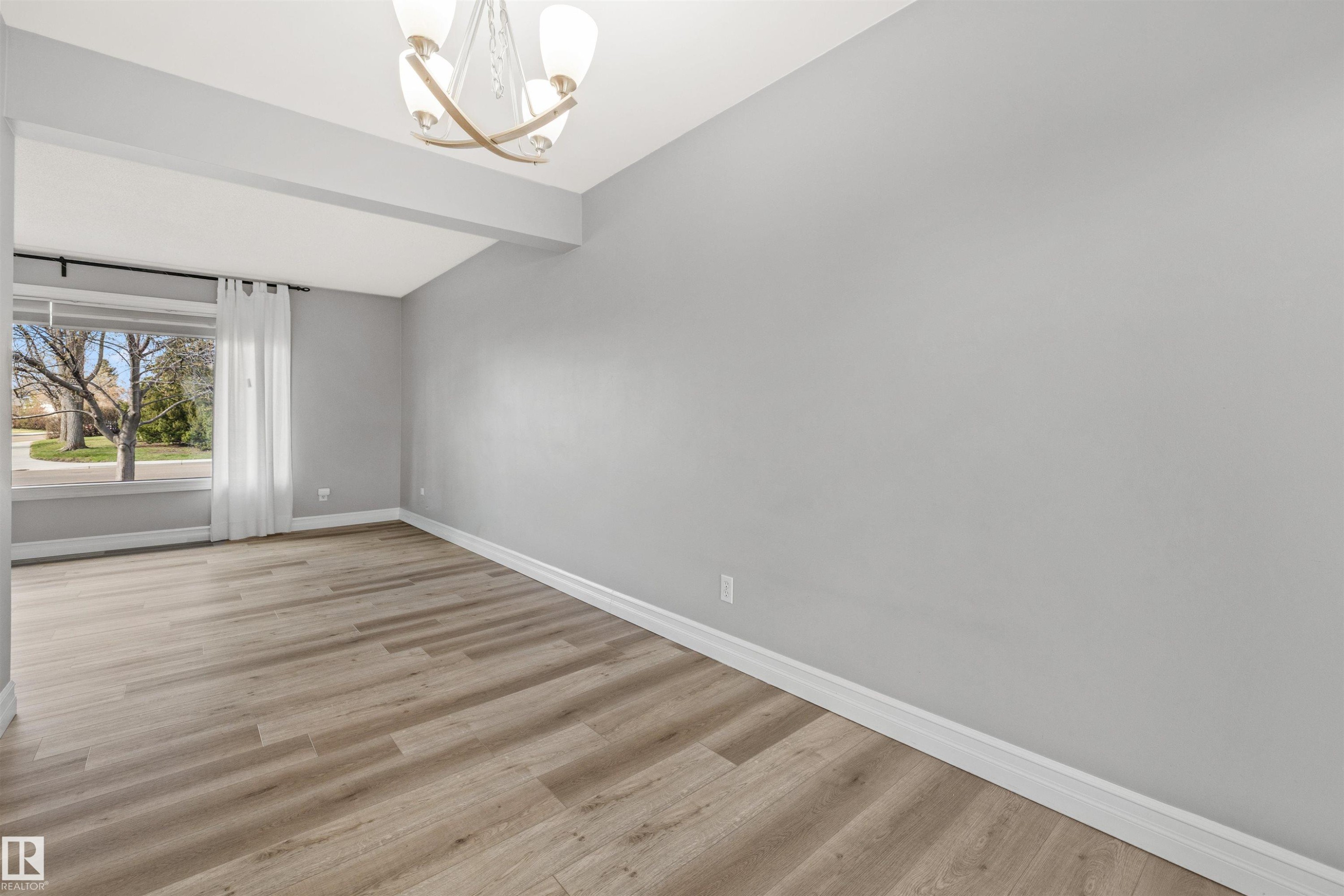 Spacious room featuring wood-finish flooring, light gray wall paint, and white baseboards - 7927 71 Avenue, Edmonton, AB - Indoor Photo Showing Other Room