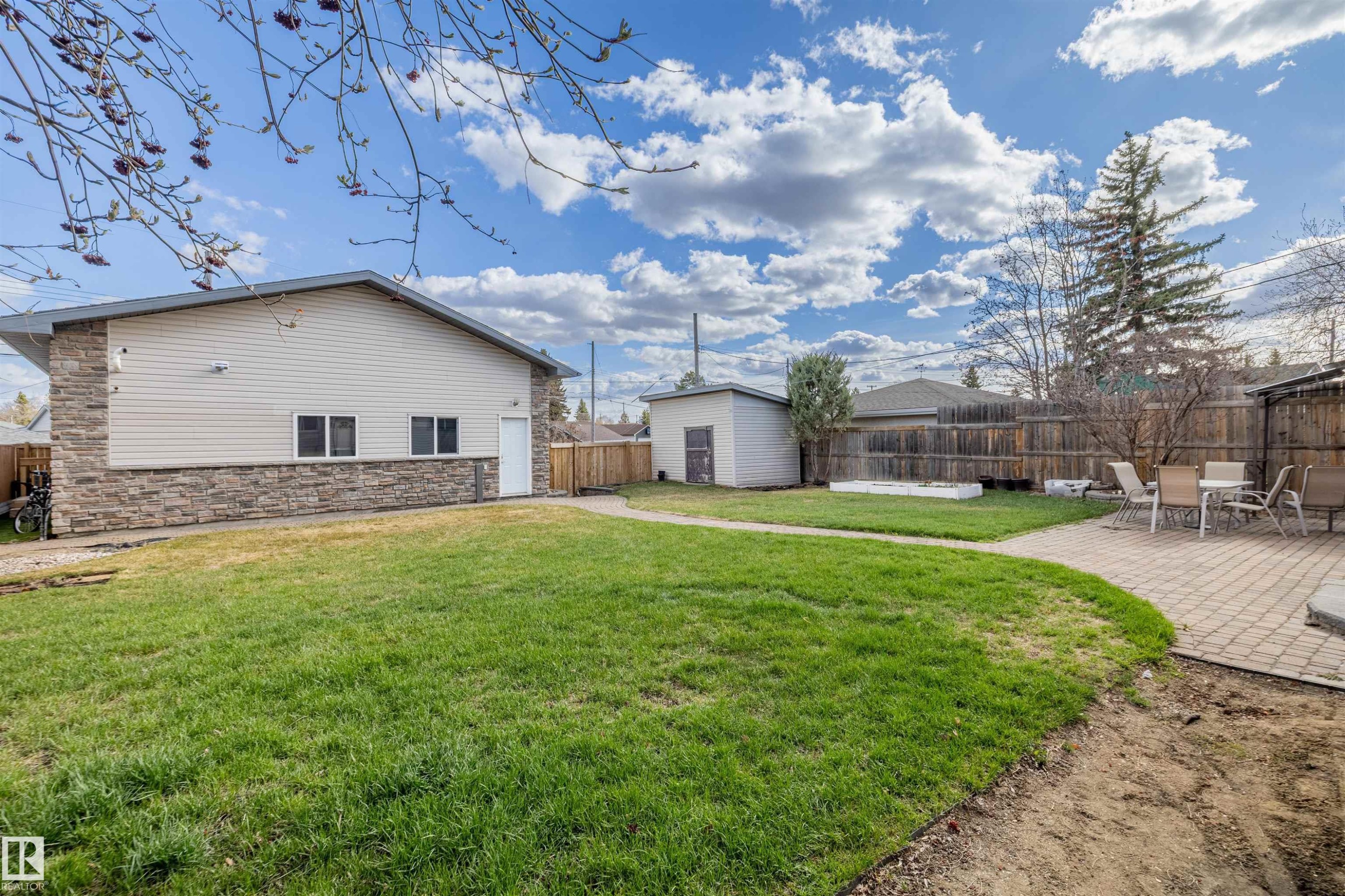 Expansive backyard featuring a manicured lawn, a paver patio area, a detached storage shed, a wood fence perimeter, and a stone-clad and siding exterior - 7927 71 Avenue, Edmonton, AB - Outdoor