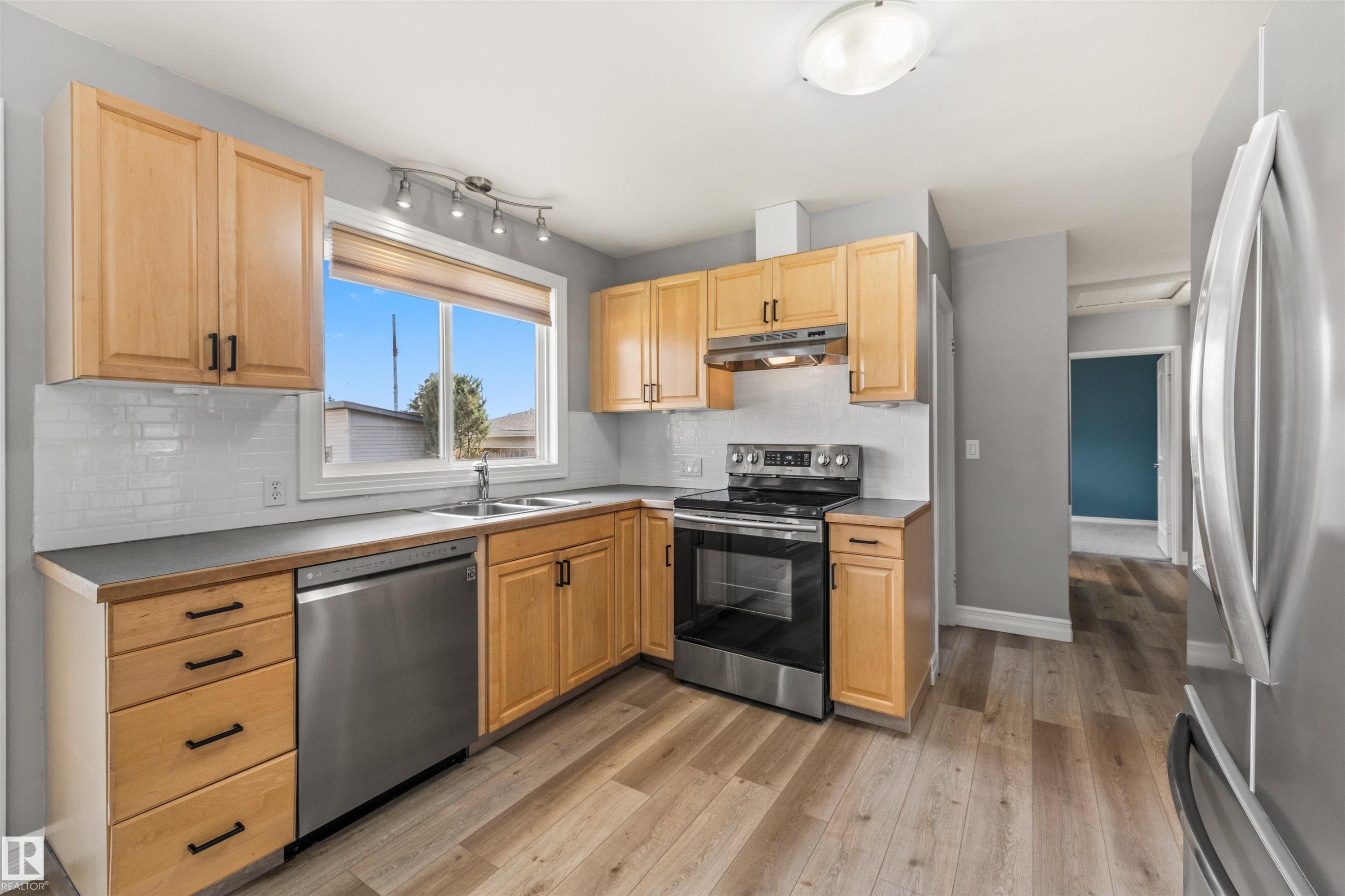 Kitchen featuring wood-finish cabinetry with black hardware, stainless steel appliances, a tile backsplash, and wood-finish flooring - 7927 71 Avenue, Edmonton, AB - Indoor Photo Showing Kitchen With Double Sink