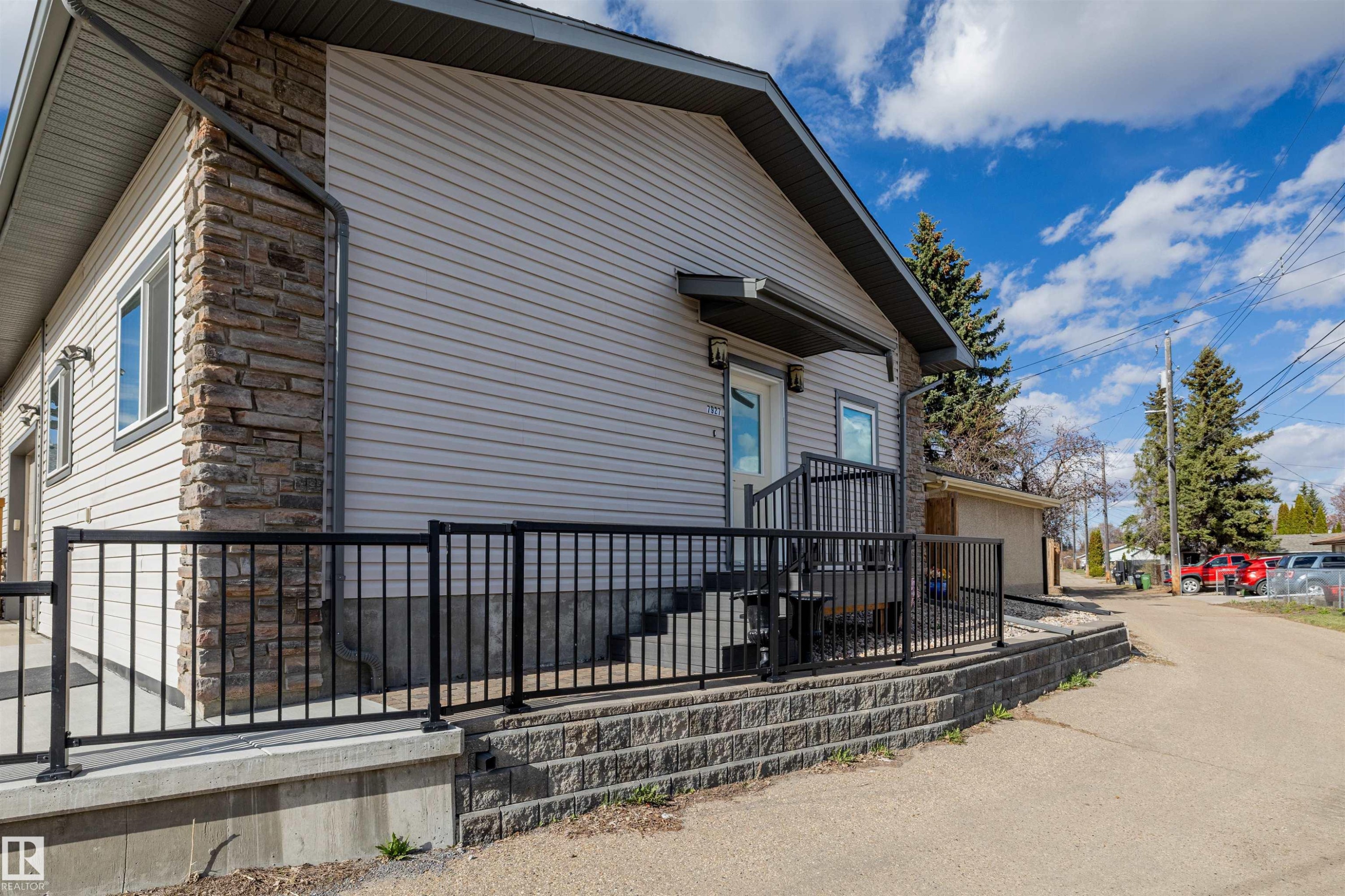 Exterior featuring light grey siding with stone veneer accents, black metal railings, a concrete foundational platform, and a paved side access - 7927 71 Avenue, Edmonton, AB - Outdoor