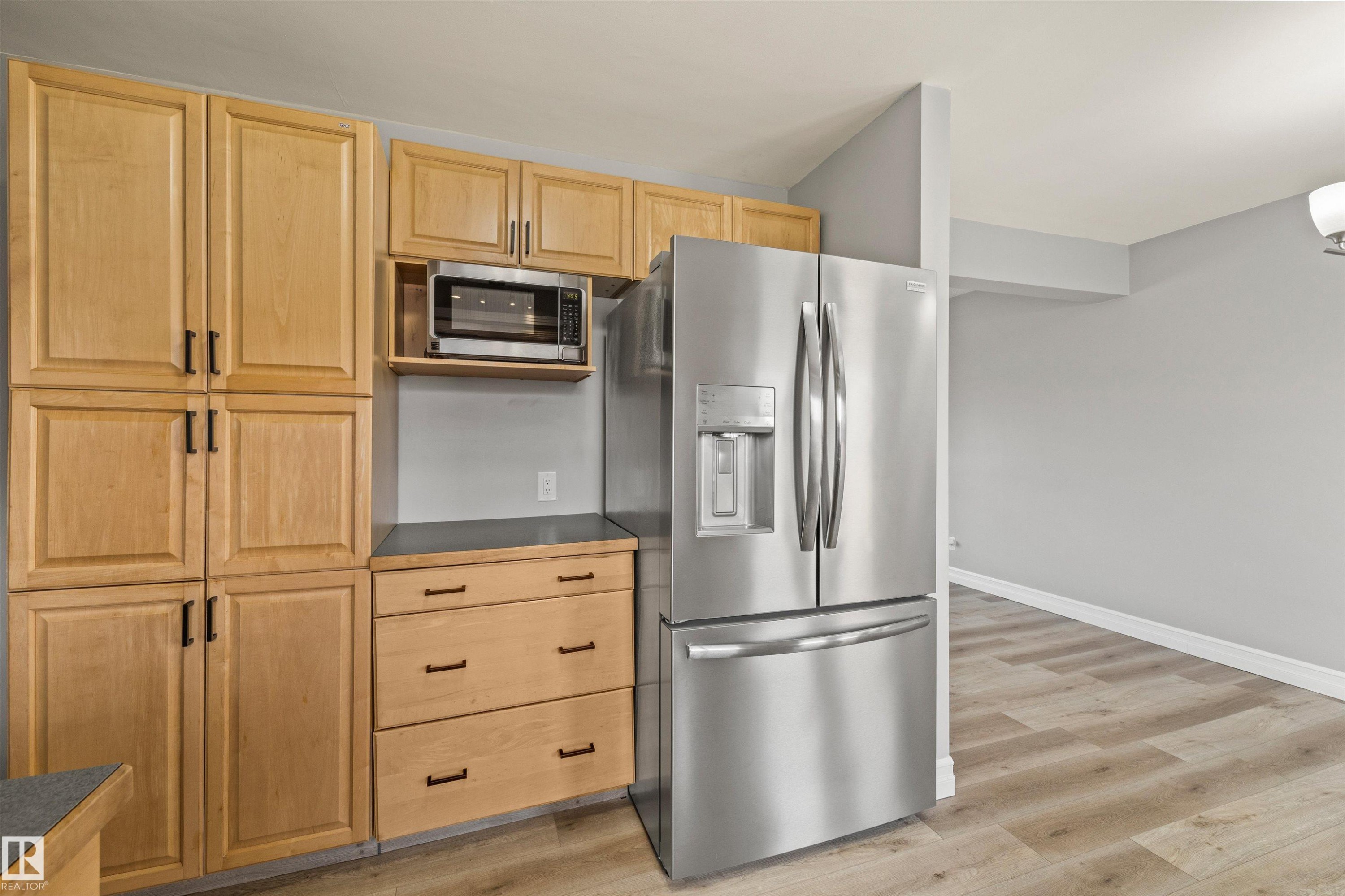 Stainless steel French door refrigerator, wood-finish flooring, light wood cabinetry, integrated microwave, and dark countertop - 7927 71 Avenue, Edmonton, AB - Indoor Photo Showing Kitchen