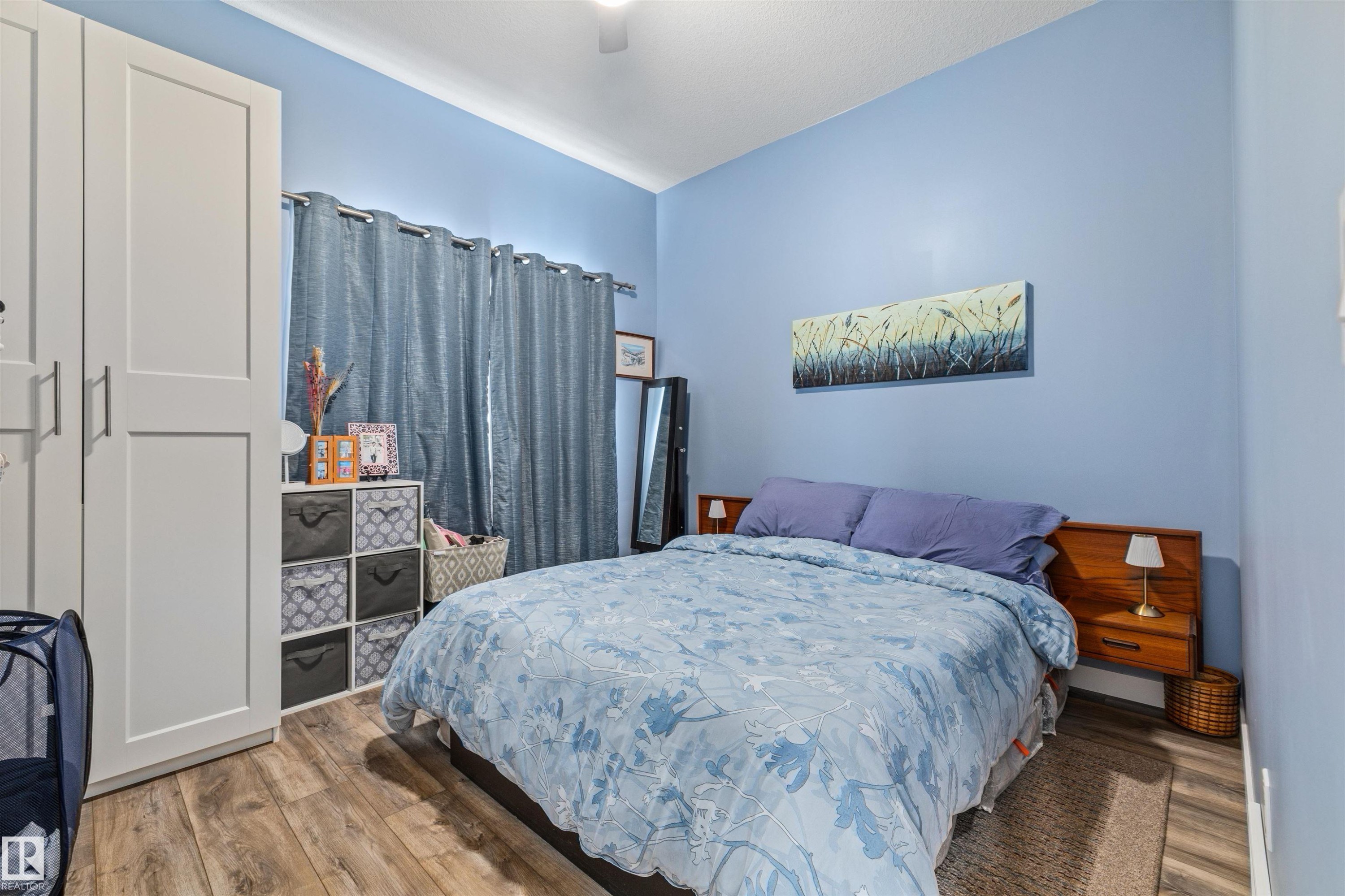 Bedroom featuring wood-finish flooring, built-in white wardrobe with shaker-style doors, and light blue walls - 7927 71 Avenue, Edmonton, AB - Indoor Photo Showing Bedroom