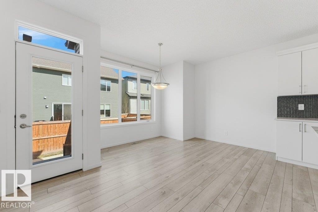 Open-concept area featuring light wood-finish flooring, a full-light exterior door with transom window, and a wall of windows - 2011 207 Street, Edmonton, AB - Indoor