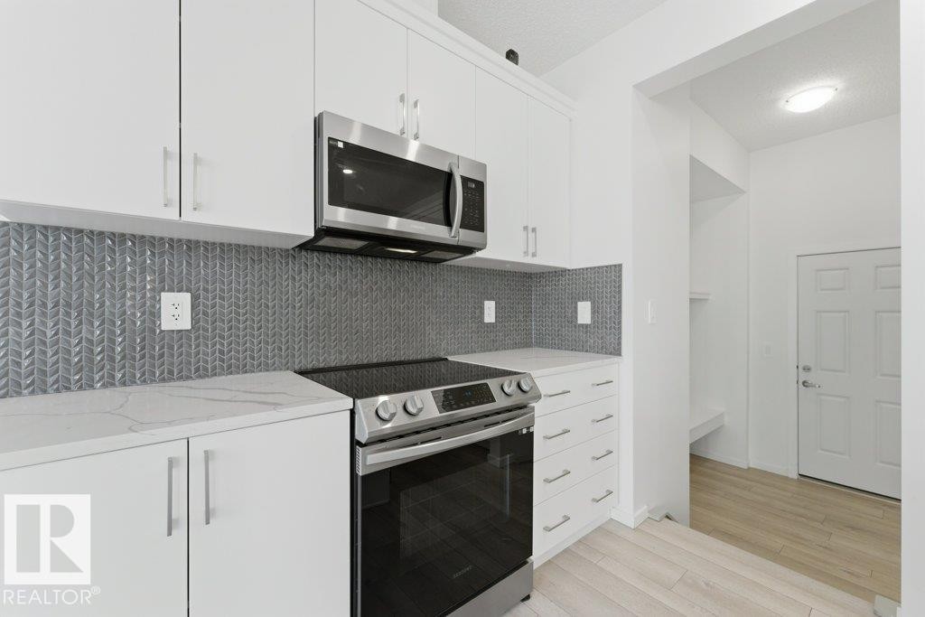 Modern kitchen featuring white cabinetry, a stainless steel range, and a coordinating stainless steel microwave - 2011 207 Street, Edmonton, AB - Indoor Photo Showing Kitchen