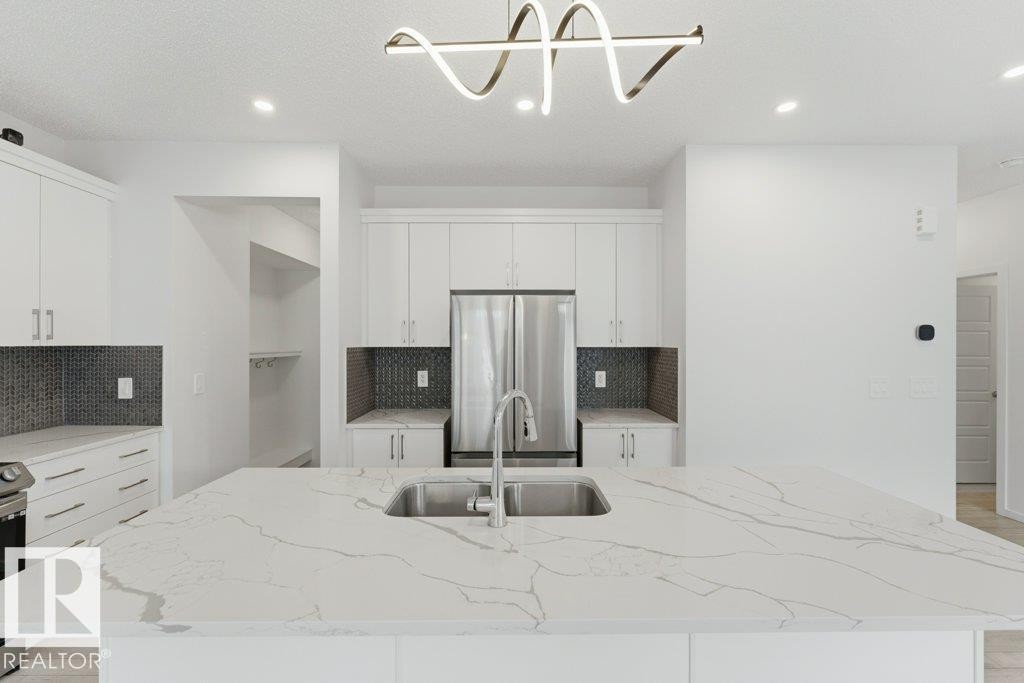 Kitchen island featuring a stainless steel undermount sink, a contemporary faucet, and a light-toned countertop with veining - 2011 207 Street, Edmonton, AB - Indoor Photo Showing Kitchen With Double Sink With Upgraded Kitchen
