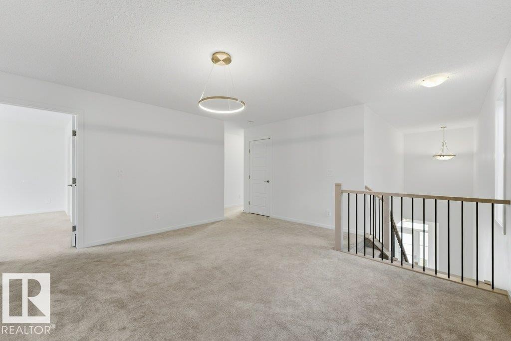 Carpeted upper-level landing featuring a modern circular pendant light, a light wood-finish and black metal baluster railing, and white interior doors - 2011 207 Street, Edmonton, AB - Indoor Photo Showing Other Room