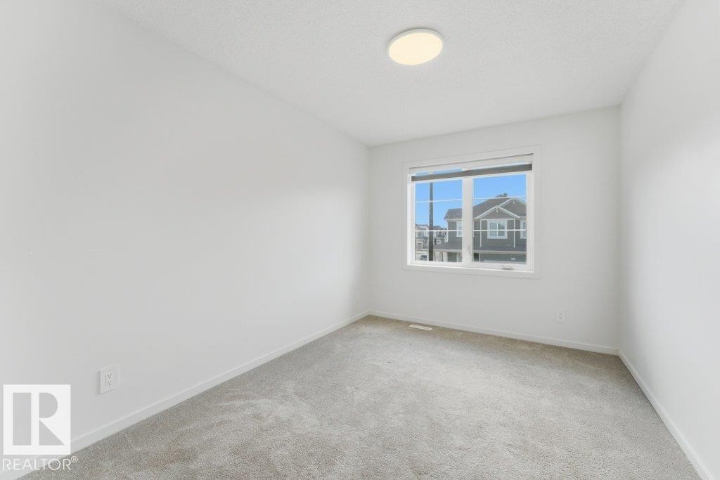 Carpeted room featuring a large window, white walls, white trim, and a ceiling-mounted light fixture - 2011 207 Street, Edmonton, AB - Indoor Photo Showing Other Room