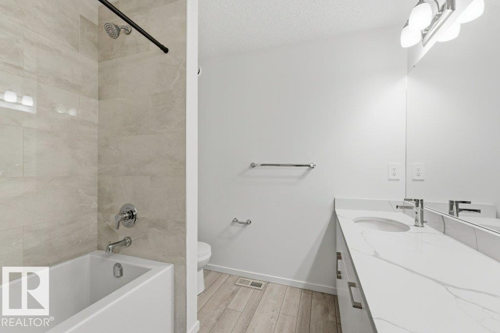 Modern bathroom featuring a white bathtub with chrome fixtures, large format tiled shower surround, a vanity with a white countertop and integrated sink, chrome faucet, and wood-finish flooring - 2011 207 Street, Edmonton, AB - Indoor Photo Showing Bathroom