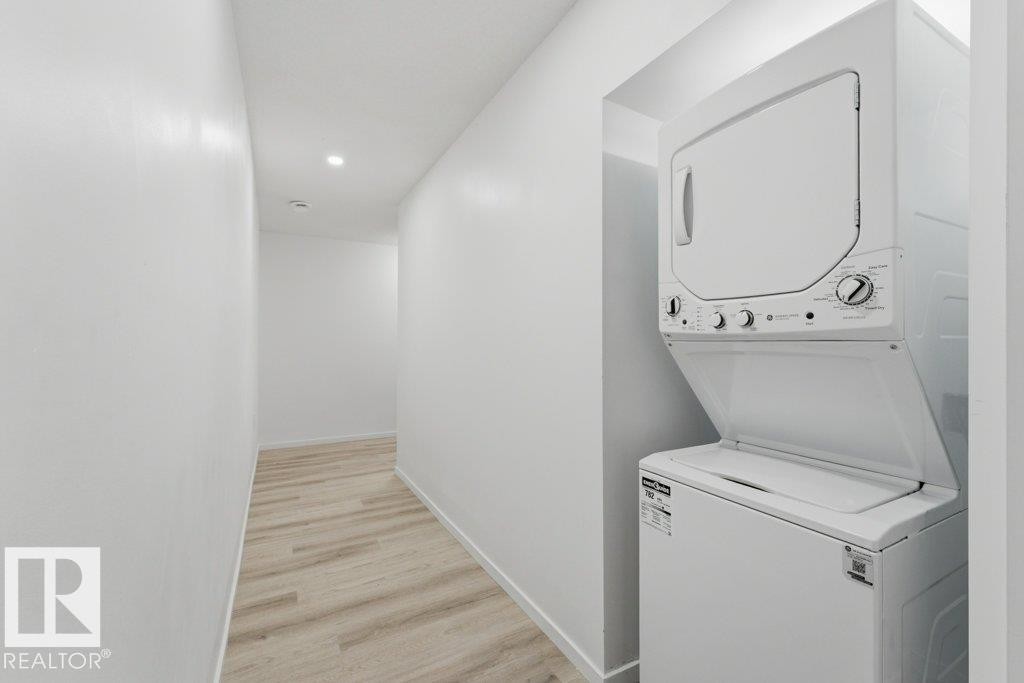 Stackable washer and dryer unit integrated into a hallway alcove featuring recessed lighting and wood-finish flooring - 2011 207 Street, Edmonton, AB - Indoor Photo Showing Laundry Room