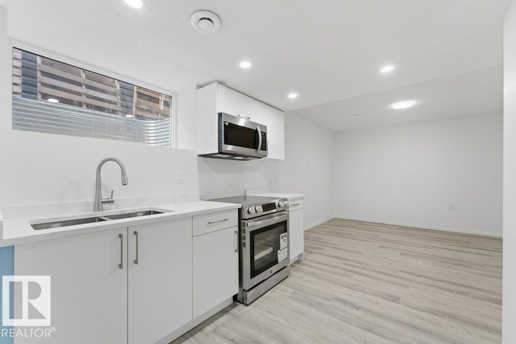 Contemporary kitchen area featuring wood-finish flooring, white cabinetry, a stainless steel double sink with a gooseneck faucet, white countertops, and recessed ceiling lighting - 2011 207 Street, Edmonton, AB - Indoor Photo Showing Kitchen With Double Sink With Upgraded Kitchen