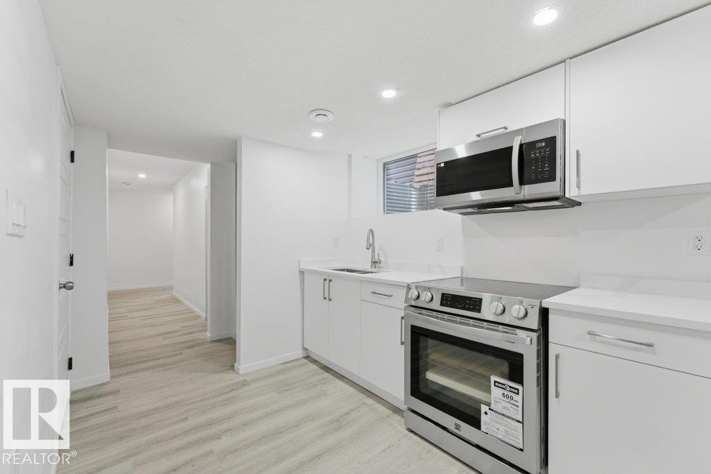 Modern kitchen featuring white cabinetry, light-toned countertops, stainless steel appliances, and recessed lighting - 2011 207 Street, Edmonton, AB - Indoor Photo Showing Kitchen