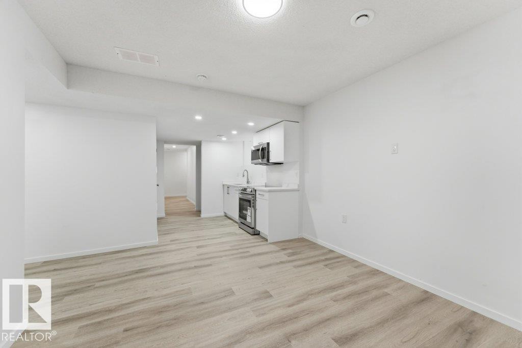 Open-concept living space with wood-finish flooring, recessed lighting, and a compact kitchen - 2011 207 Street, Edmonton, AB - Indoor Photo Showing Other Room