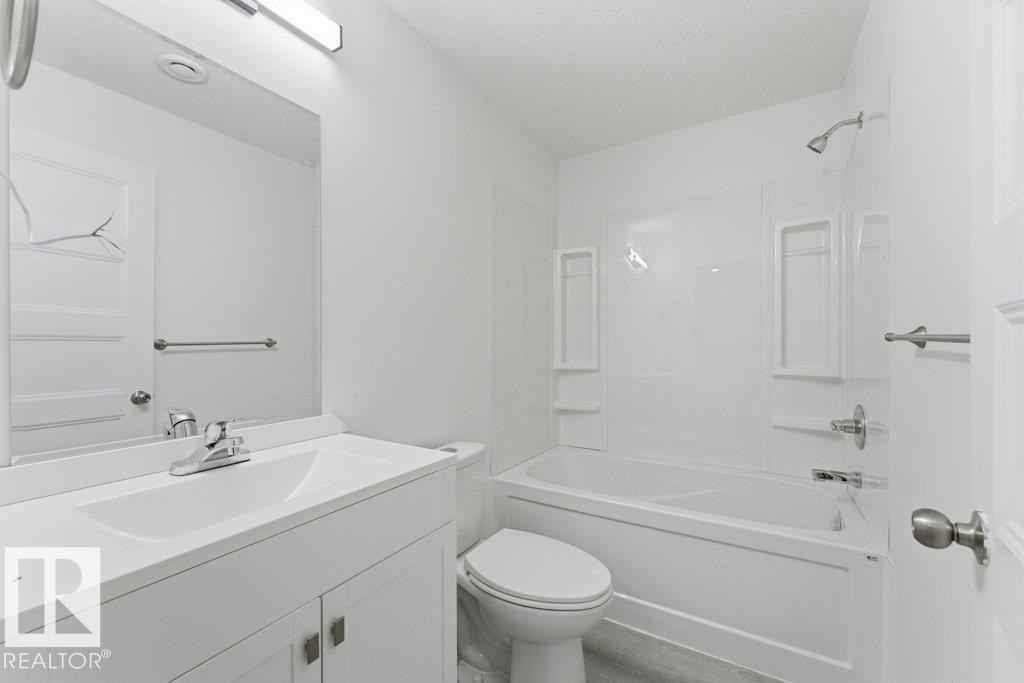 Bathroom featuring a white vanity with an integrated sink, chrome faucet, and a rectangular mirror with an overhead light fixture - 2011 207 Street, Edmonton, AB - Indoor Photo Showing Bathroom