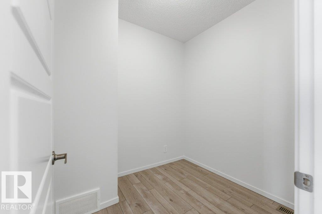 Neutral tone interior featuring wood-finish flooring, white baseboards, and a paneled door with brushed nickel hardware - 2011 207 Street, Edmonton, AB - Indoor Photo Showing Other Room