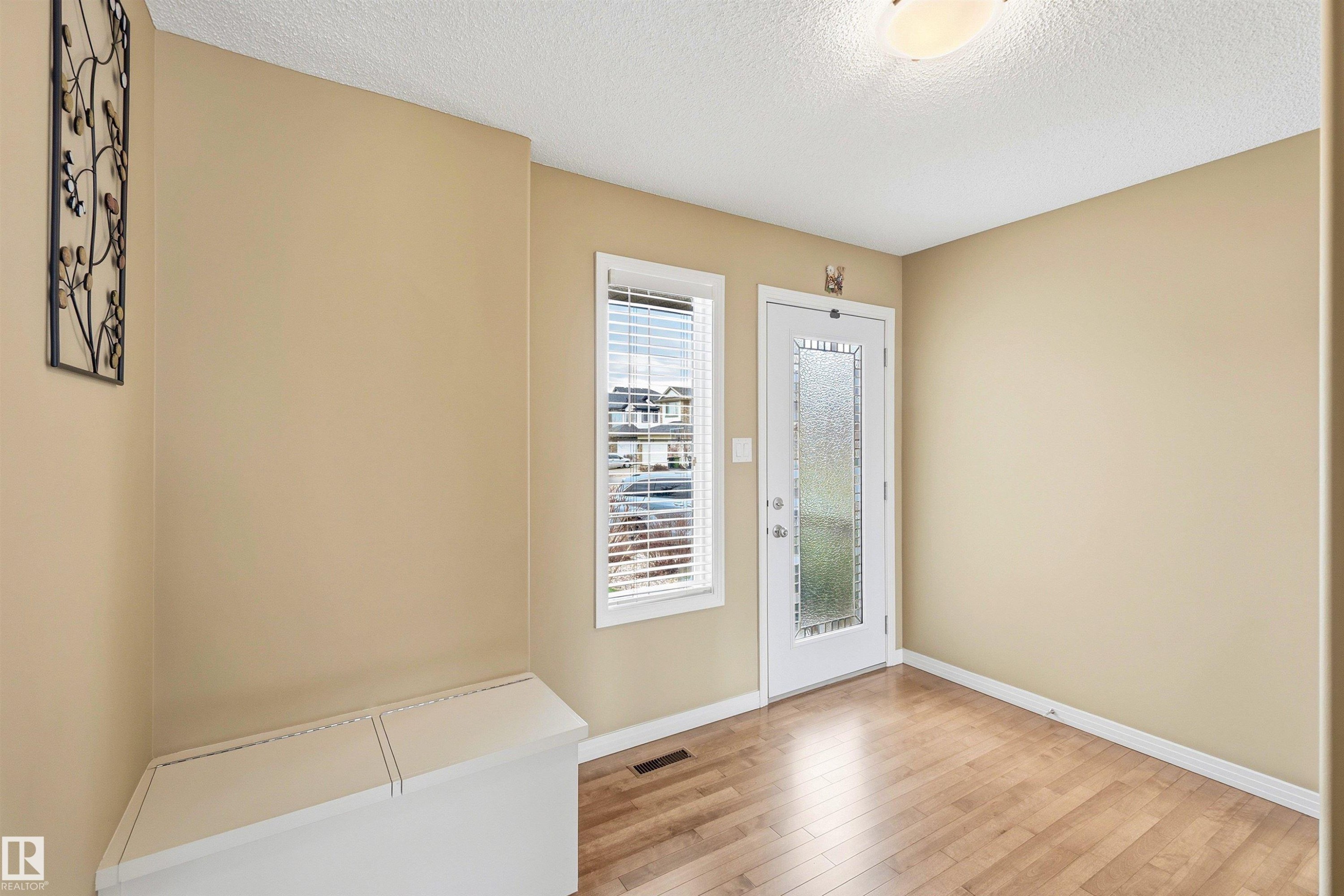 Entryway featuring wood-finish flooring, a full-lite exterior door with privacy glass, a single window with blinds, and a flush-mount ceiling light fixture - 2340 Hagen Link, Edmonton, AB - Indoor Photo Showing Other Room