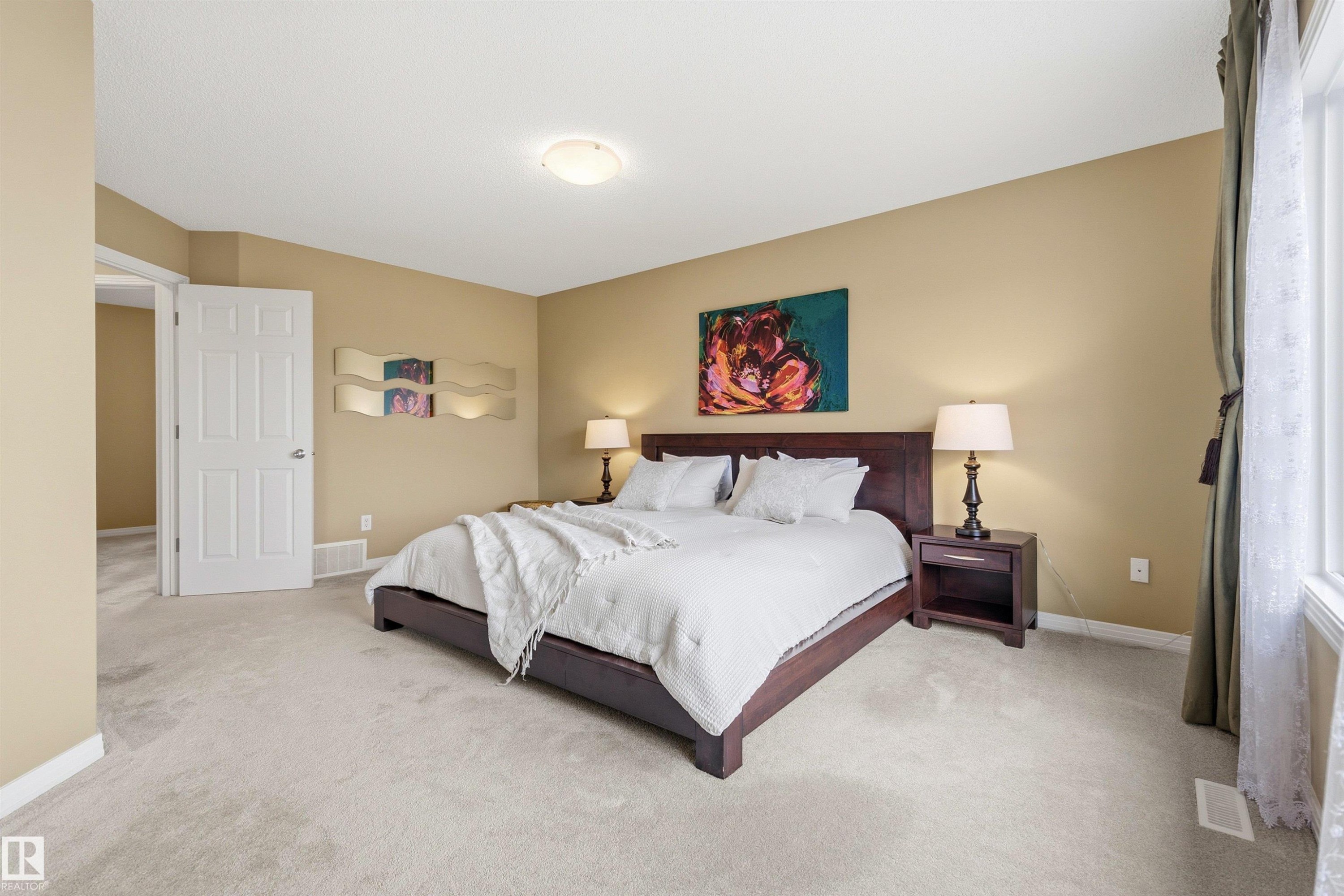 Spacious bedroom featuring light-toned carpeting, a built-in window, a white paneled door, a ceiling-mounted light fixture, and neutral wall tones - 2340 Hagen Link, Edmonton, AB - Indoor Photo Showing Bedroom