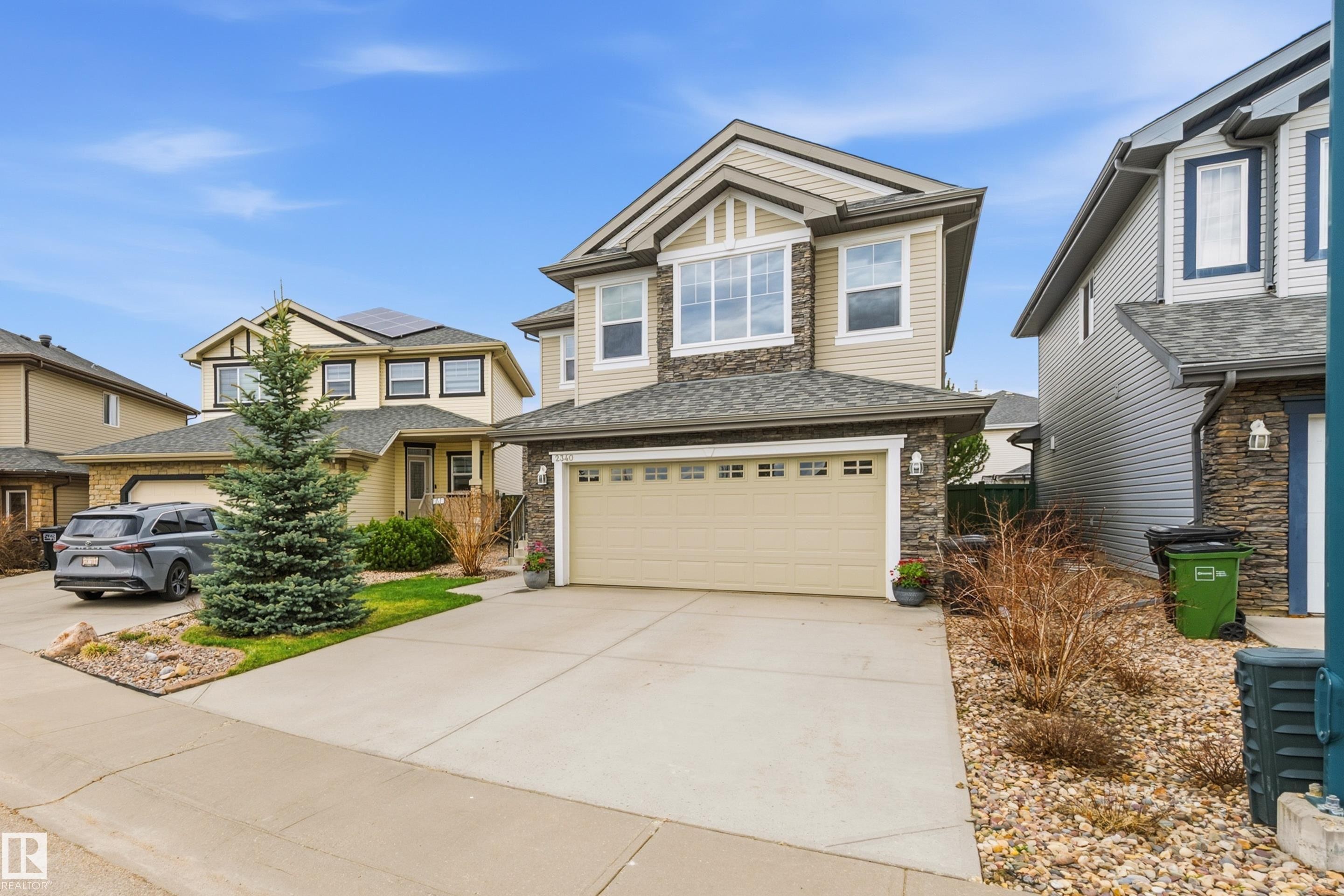 Two-story residence featuring a neutral siding exterior with stone accents, a dual garage door, and a prominent front-facing bay window - 2340 Hagen Link, Edmonton, AB - Outdoor With Facade