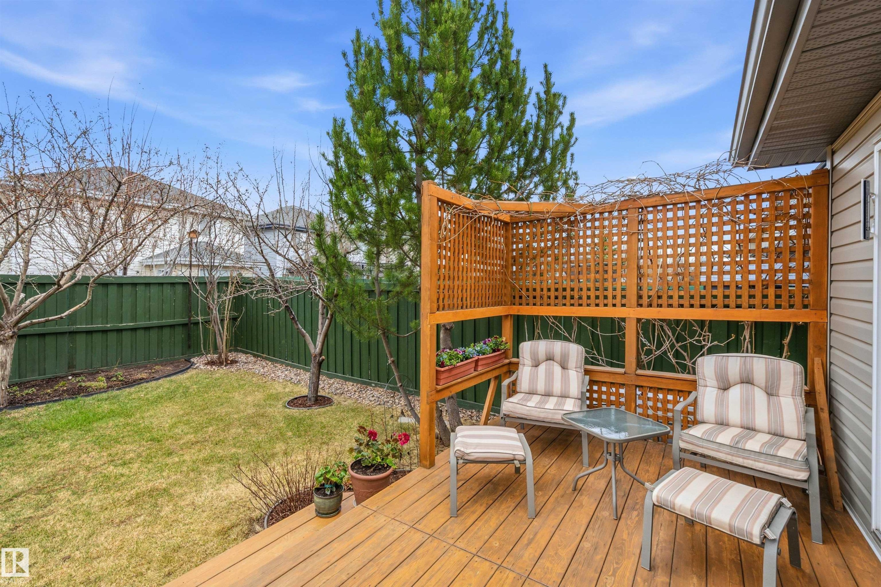 Expansive wooden deck featuring a built-in lattice privacy screen and direct access to a green-fenced yard with mature trees and landscaping - 2340 Hagen Link, Edmonton, AB - Outdoor With Deck Patio Veranda