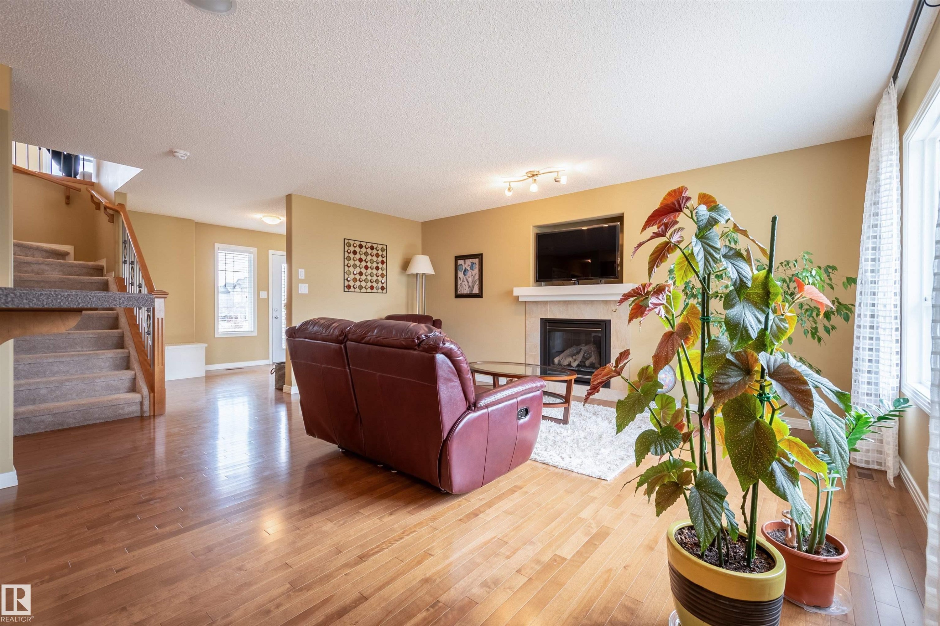 Spacious living area featuring wood-finish flooring, a carpeted staircase with a wood and metal railing, and a fireplace with a mantel - 2340 Hagen Link, Edmonton, AB - Indoor Photo Showing Living Room With Fireplace
