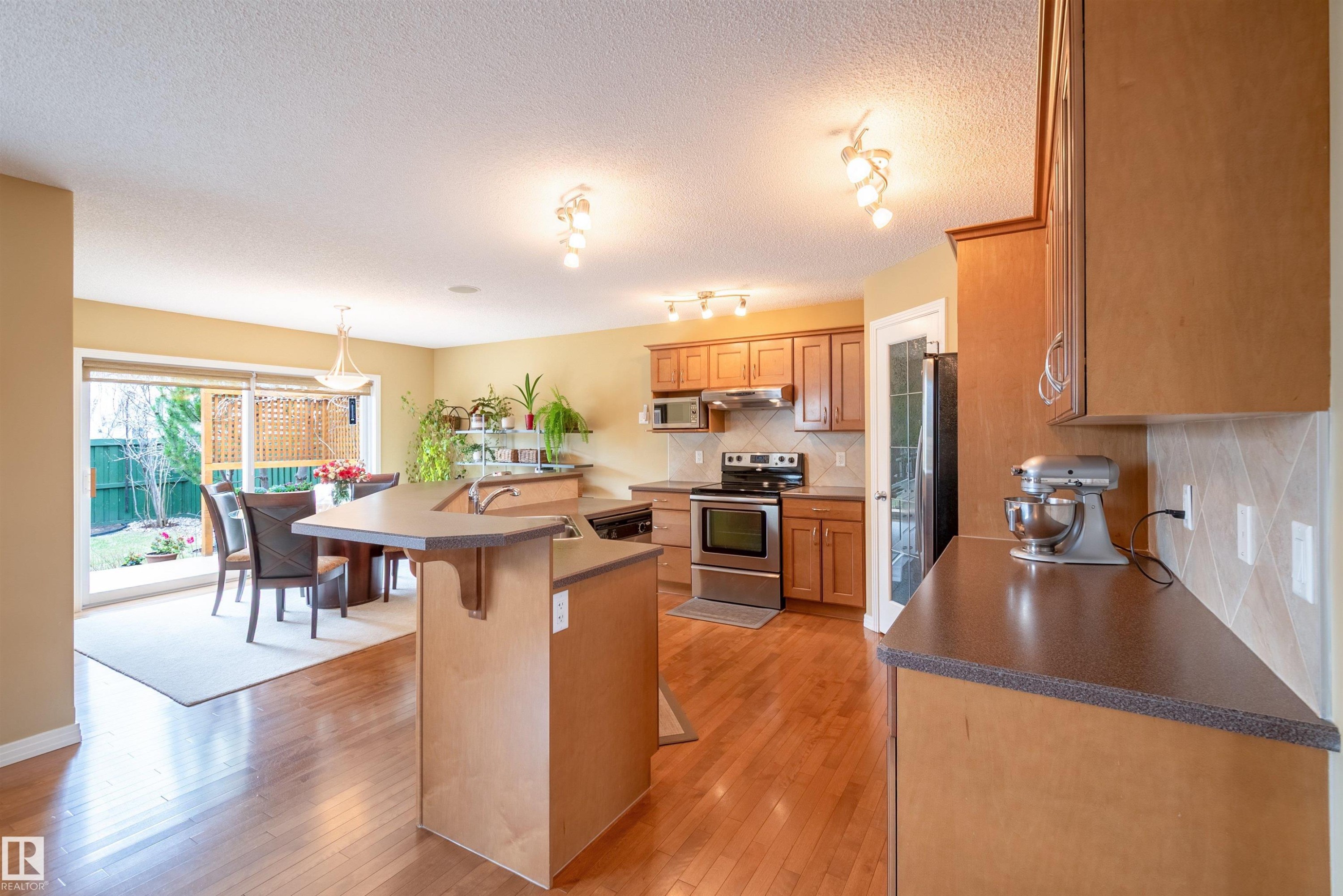 Kitchen featuring wood-finish flooring, light-toned cabinetry, stainless steel appliances, and a breakfast bar - 2340 Hagen Link, Edmonton, AB - Indoor Photo Showing Kitchen