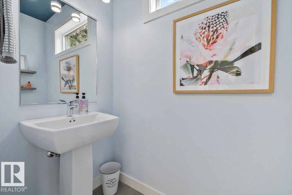 Pedestal sink featuring a chrome faucet, wall-mounted mirror, and wood-finish flooring - 11245 64 Street, Edmonton, AB - Indoor Photo Showing Bathroom