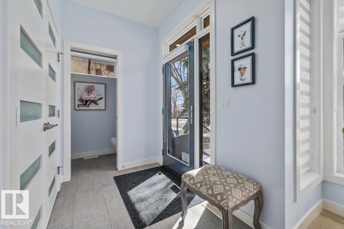 Entryway featuring light gray tile flooring, a modern glass-paneled entry door, white interior doors with frosted glass inserts, and a powder room with a transom window - 11245 64 Street, Edmonton, AB - Indoor Photo Showing Other Room