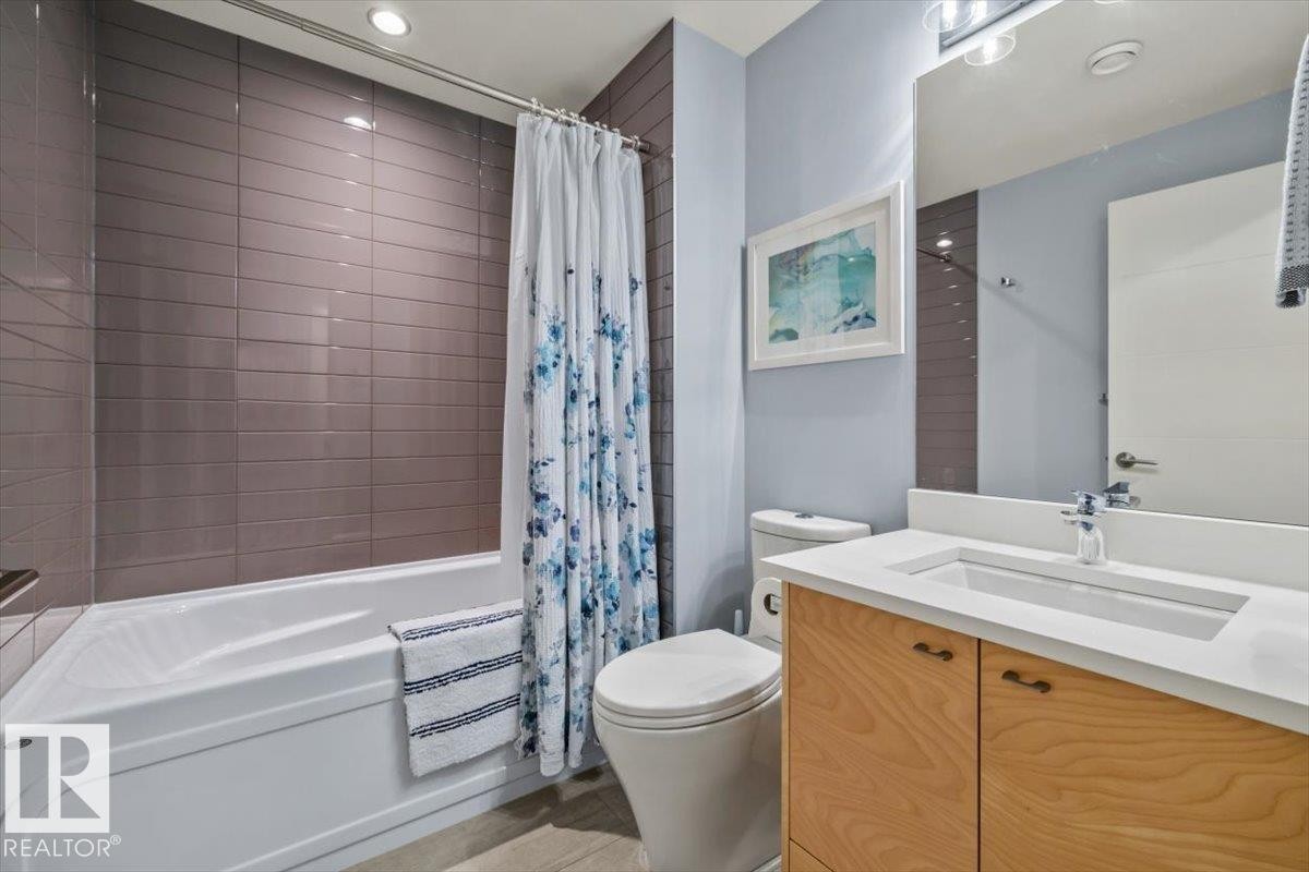 Bathroom featuring a white bathtub with subway tile surround, wood-finish vanity with an integrated sink, and an overhead vanity light fixture - 11245 64 Street, Edmonton, AB - Indoor Photo Showing Bathroom