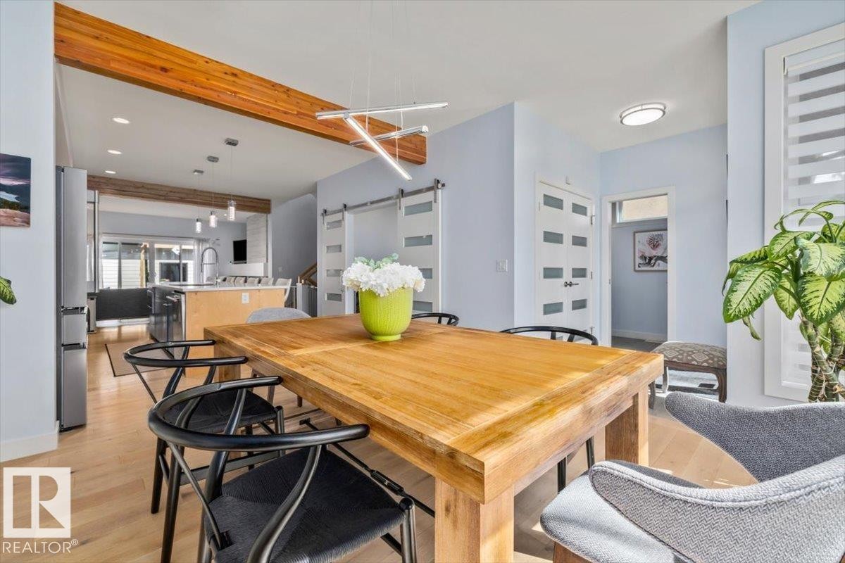 Open-concept dining area featuring wood-finish flooring, a modern linear chandelier, and exposed wood ceiling beams - 11245 64 Street, Edmonton, AB - Indoor Photo Showing Dining Room