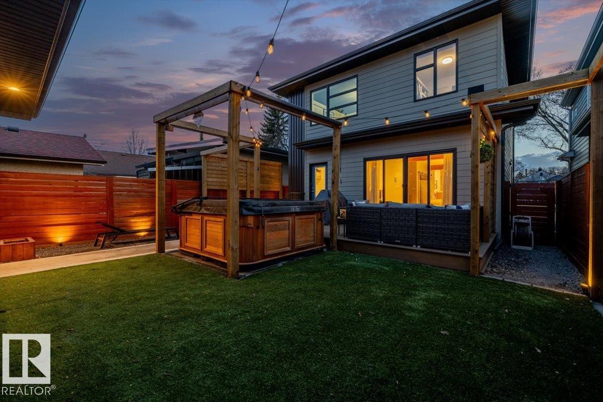 Private backyard featuring a hot tub within a wooden pergola, artificial turf lawn, and a deck with sliding glass doors - 11245 64 Street, Edmonton, AB - Outdoor