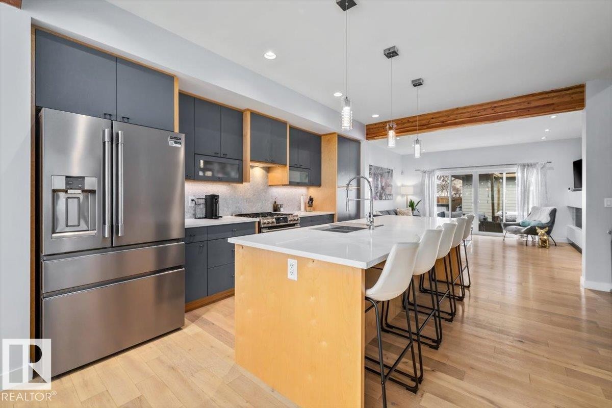 Contemporary kitchen featuring integrated stainless steel appliances, dark gray cabinetry with light wood accents, a white subway tile backsplash, and a large island with a white countertop - 11245 64 Street, Edmonton, AB - Indoor Photo Showing Kitchen With Upgraded Kitchen