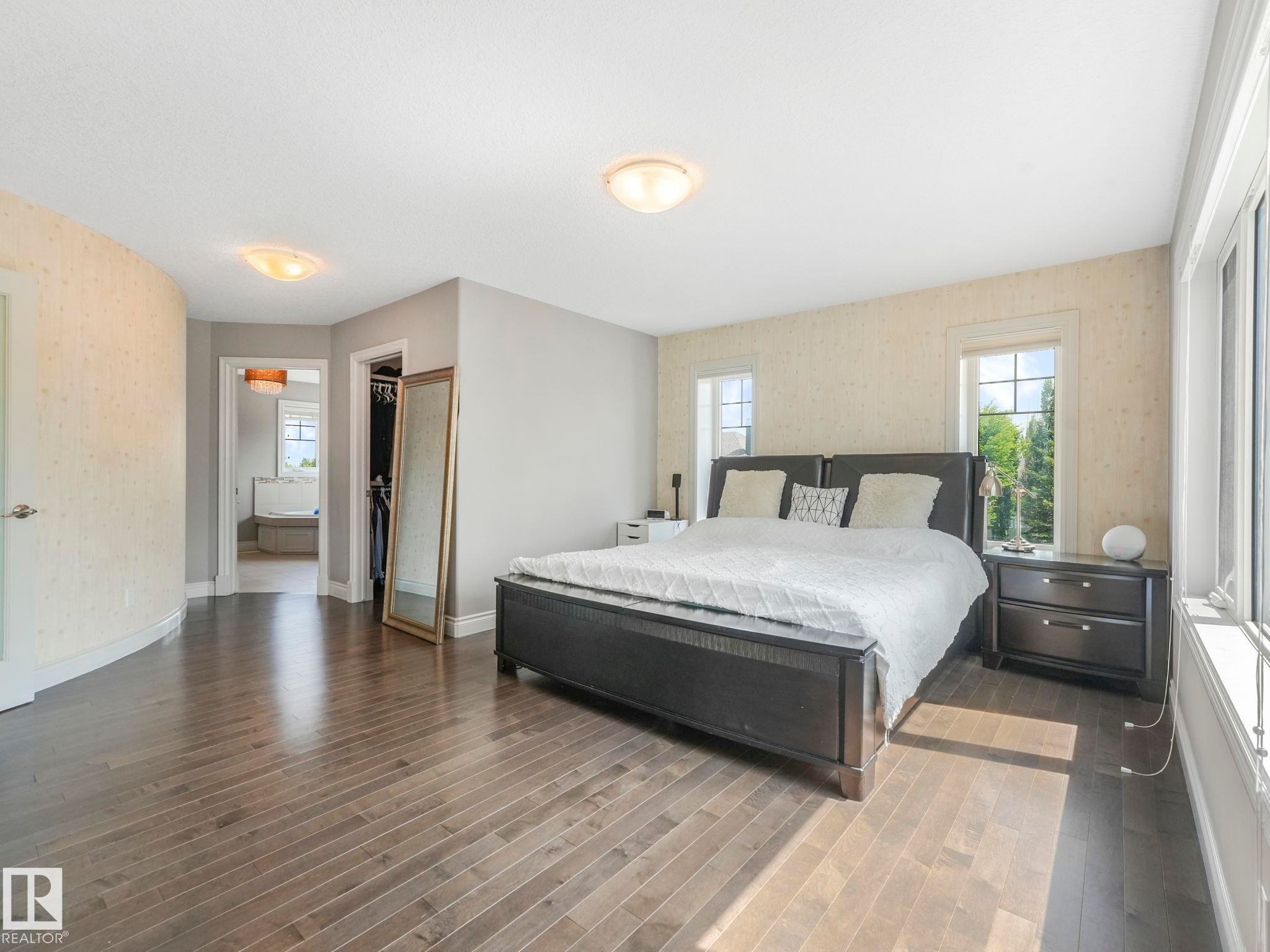 Spacious bedroom featuring wood-finish flooring, multiple windows, and a doorway opening to an additional room with a built-in tub - 932 Summerside Link, Edmonton, AB - Indoor Photo Showing Bedroom