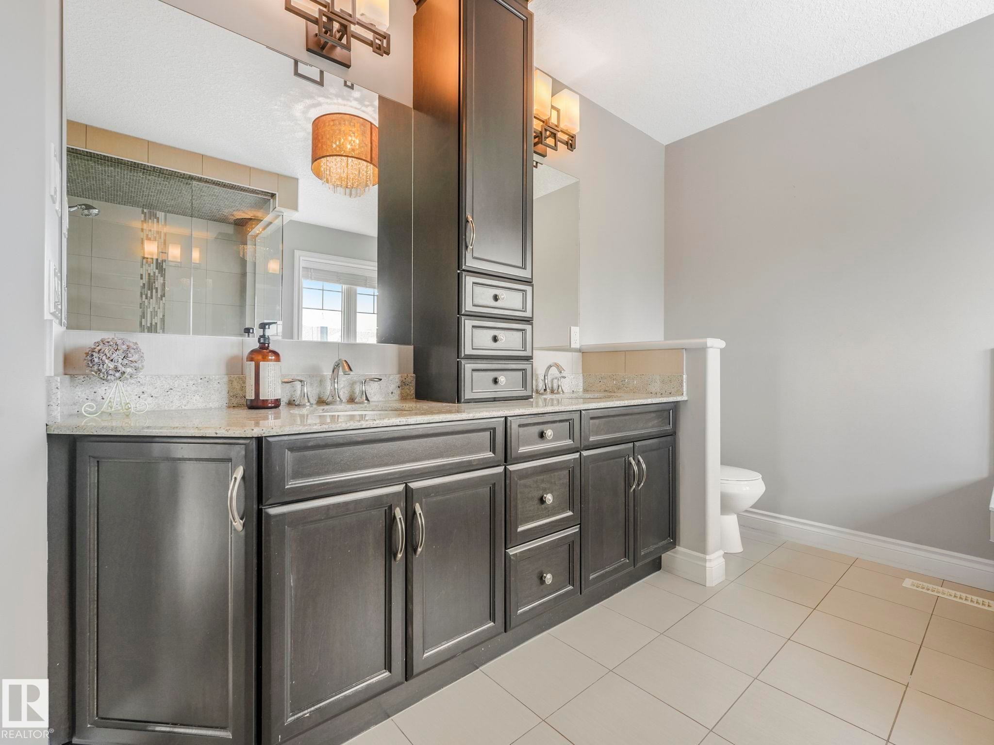 Dual vanity with granite countertop, integrated sinks, dark wood cabinetry, and a tall storage tower - 932 Summerside Link, Edmonton, AB - Indoor Photo Showing Bathroom