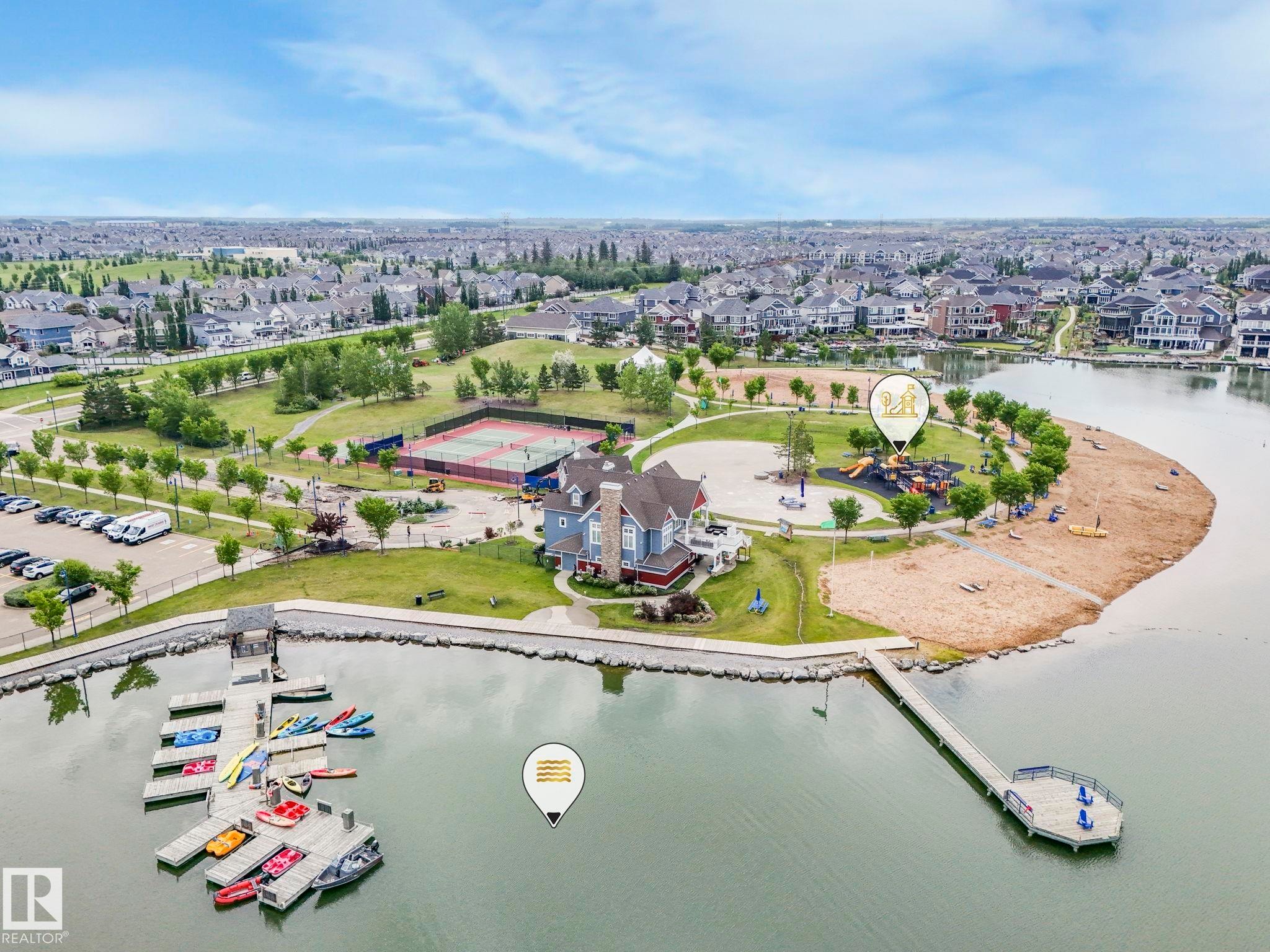 Waterfront recreational area featuring a multi-level boat dock, a sandy beach, and a children's playground - 932 Summerside Link, Edmonton, AB - Outdoor With Body Of Water With View