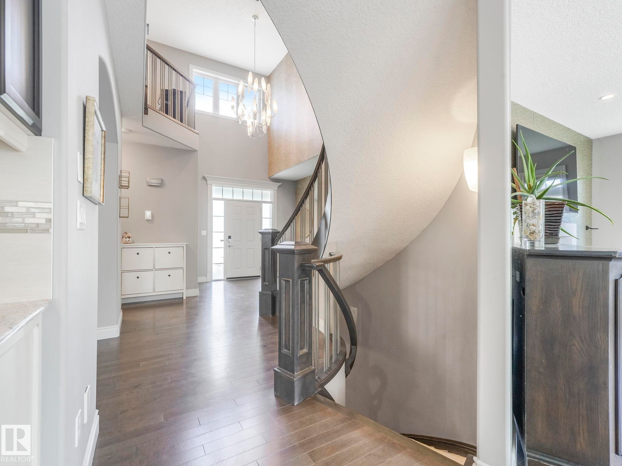 Grand foyer featuring a dark wood-finish flooring, a two-story ceiling, and a prominent curved staircase with dark wood newel posts and railings - 932 Summerside Link, Edmonton, AB - Indoor Photo Showing Other Room
