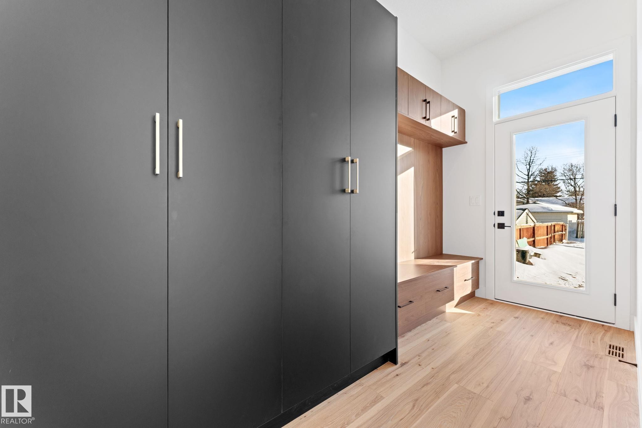 Entryway featuring light hardwood flooring, built-in storage with a wooden bench, dark grey wardrobe units with silver handles, and a glass-paneled door - 11019 132 St, Edmonton, AB - Indoor Photo Showing Other Room