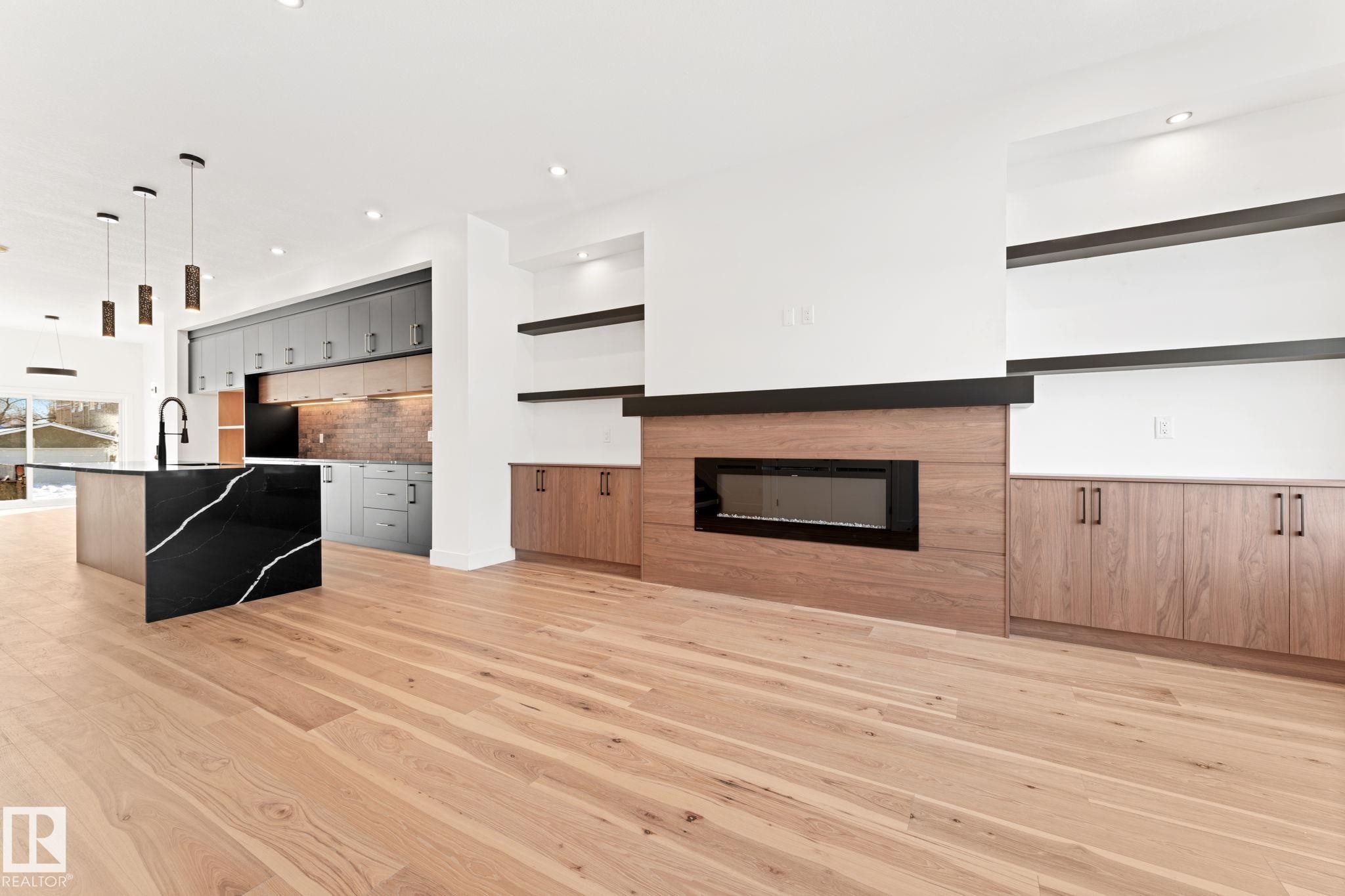 The living area features light wood flooring, a fireplace with a wood surround, and built-in shelving - 11019 132 St, Edmonton, AB - Indoor Photo Showing Living Room With Fireplace