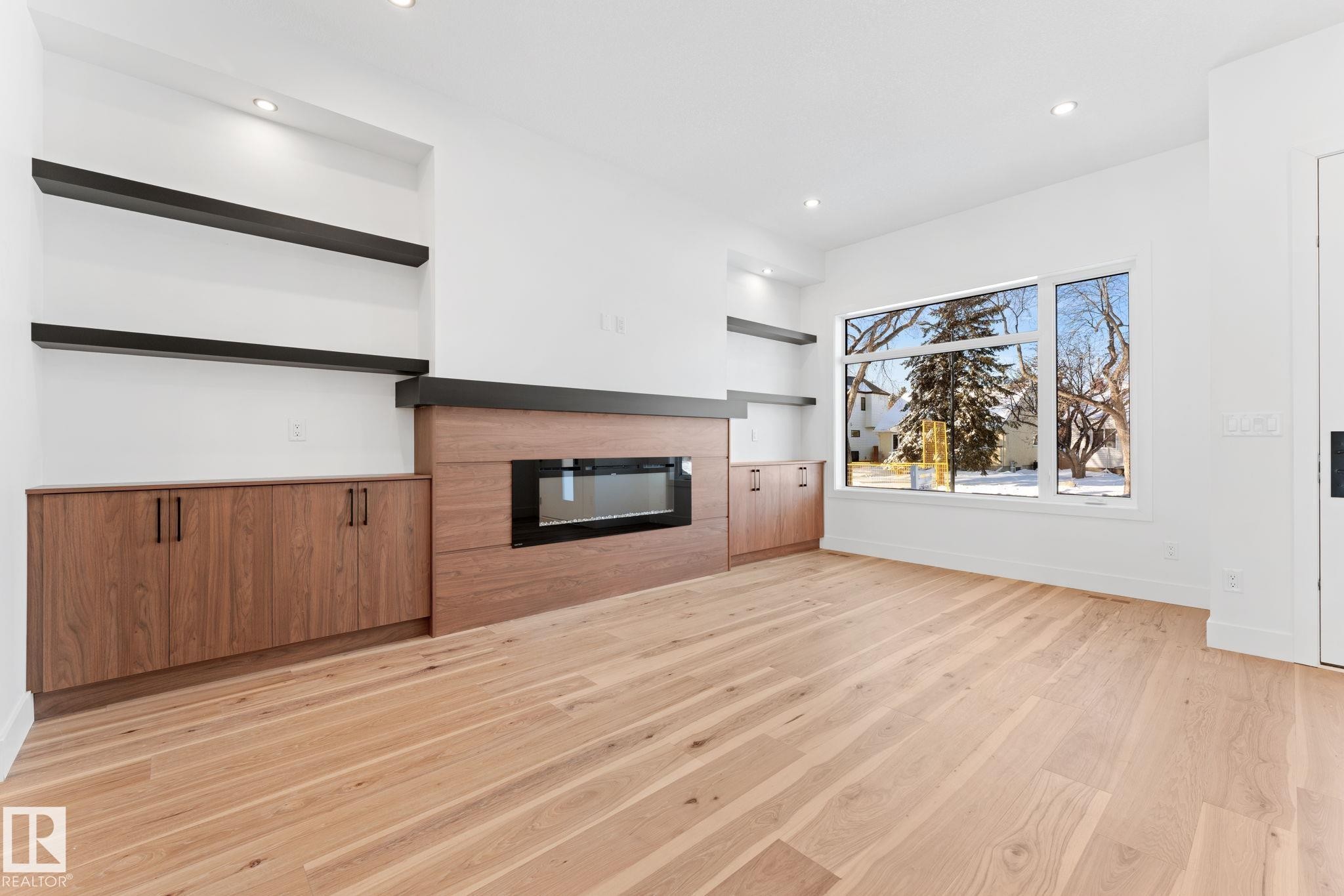 This inviting room features light hardwood floors, a contemporary fireplace, and built-in wooden cabinetry with open shelving - 11019 132 St, Edmonton, AB - Indoor Photo Showing Living Room With Fireplace