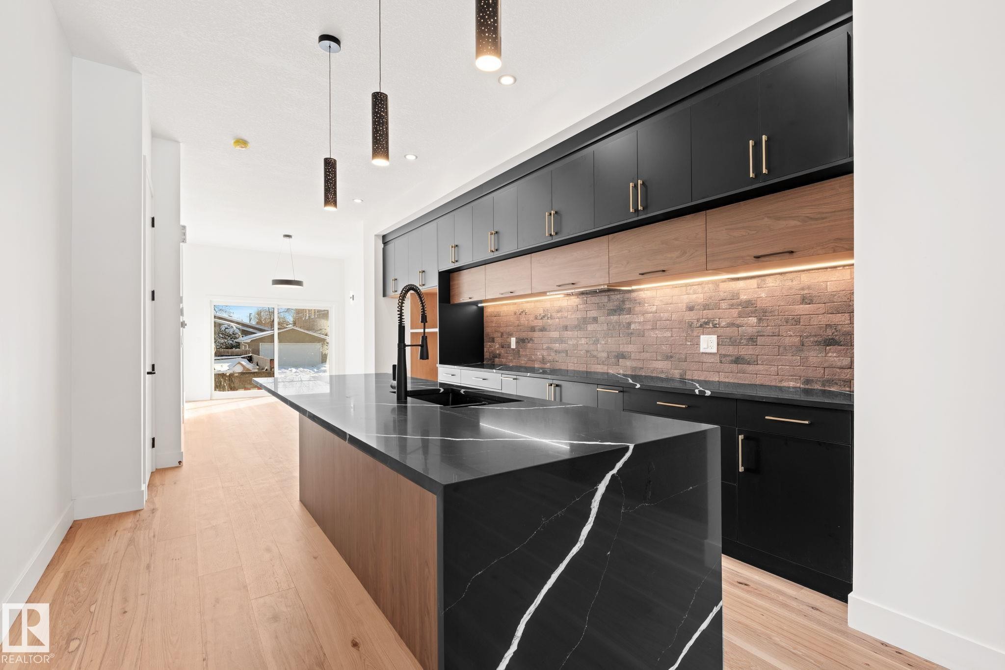 The kitchen features a striking black island with white veining, complemented by black cabinetry and wood-toned elements - 11019 132 St, Edmonton, AB - Indoor Photo Showing Kitchen With Upgraded Kitchen