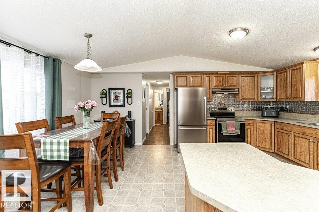 Open concept kitchen and dining area featuring wood cabinetry, stainless steel appliances, a kitchen island with ample counter space, and durable linoleum flooring - 1637 68 Avenue, Edmonton, AB - Indoor