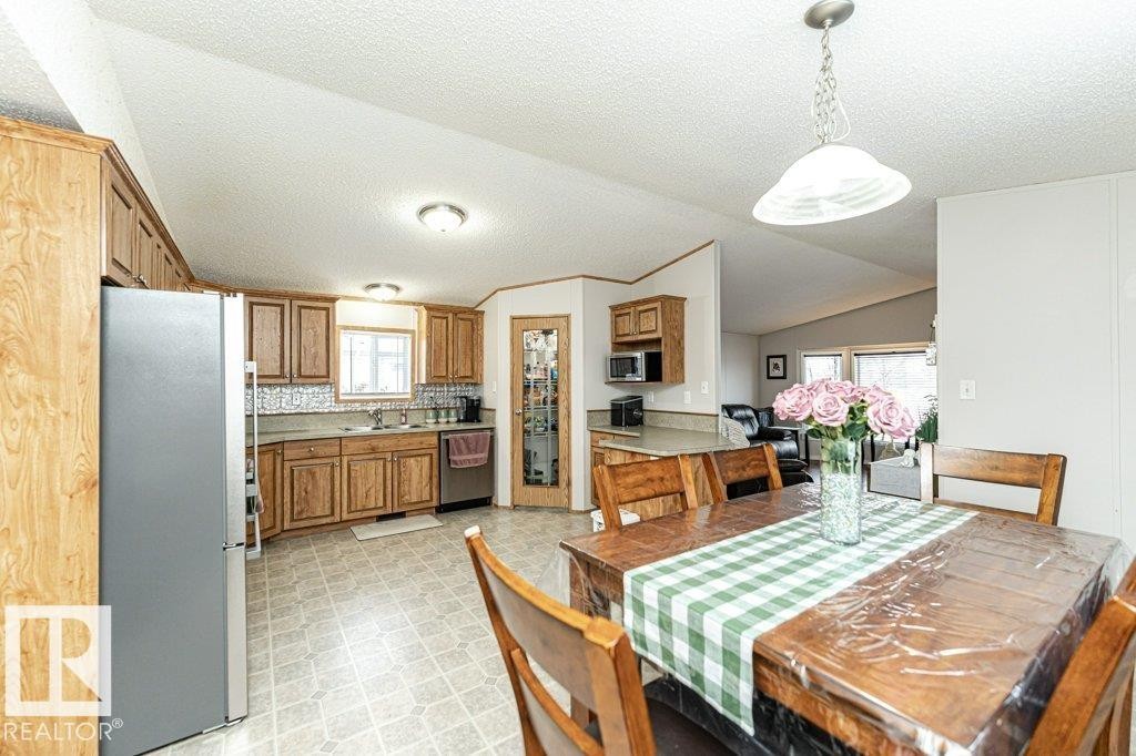 Spacious kitchen and dining area featuring wood-finish cabinetry, stainless steel appliances, a tiled backsplash, and a pantry with a glass-paneled door - 1637 68 Avenue, Edmonton, AB - Indoor Photo Showing Dining Room