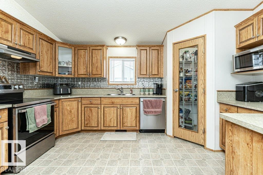 Kitchen featuring warm wood-finish cabinetry, a patterned tile backsplash, and light-toned countertops - 1637 68 Avenue, Edmonton, AB - Indoor Photo Showing Kitchen With Double Sink