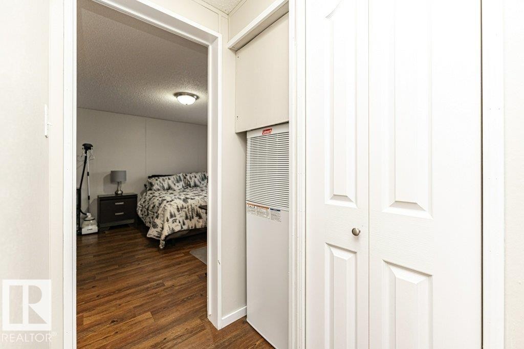 Hallway featuring bi-fold closet doors, integrated utility closet, and wood-finish flooring extending into an adjacent room - 1637 68 Avenue, Edmonton, AB - Indoor Photo Showing Other Room