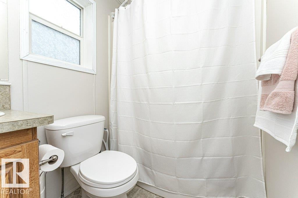 Bathroom featuring a white toilet, wood-finish vanity, and a shower with a white curtain - 1637 68 Avenue, Edmonton, AB - Indoor Photo Showing Bathroom