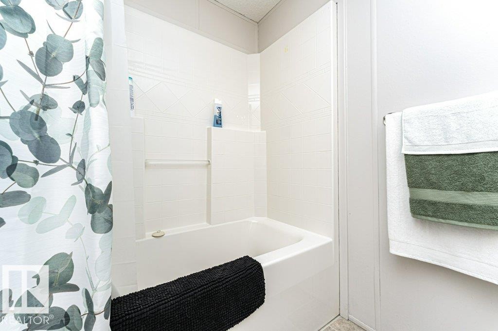 White bathtub featuring integrated shelving and a textured tile surround - 1637 68 Avenue, Edmonton, AB - Indoor Photo Showing Bathroom