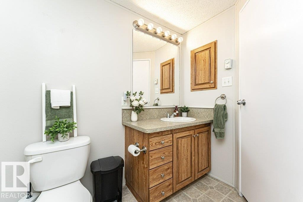 Bathroom featuring a wood-finish vanity with a built-in sink, a speckled countertop, and overhead vanity lighting - 1637 68 Avenue, Edmonton, AB - Indoor Photo Showing Bathroom