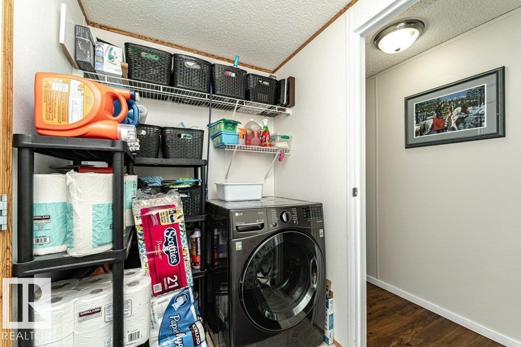 Dedicated laundry area featuring a front-loading washing machine, overhead wire shelving, and wood-finish flooring - 1637 68 Avenue, Edmonton, AB - Indoor Photo Showing Laundry Room